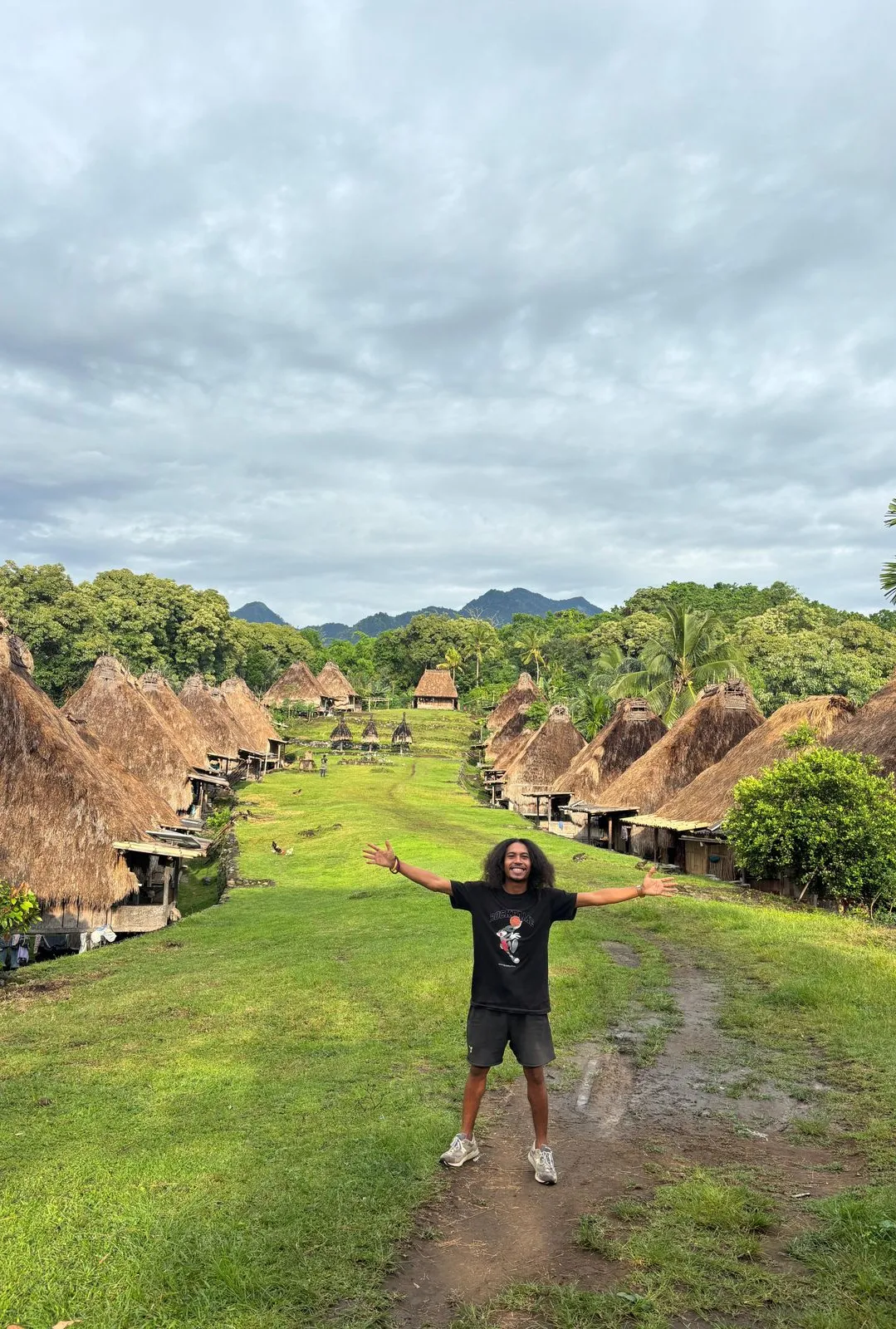 A traveller standing arms-wide in a traditional Flores village